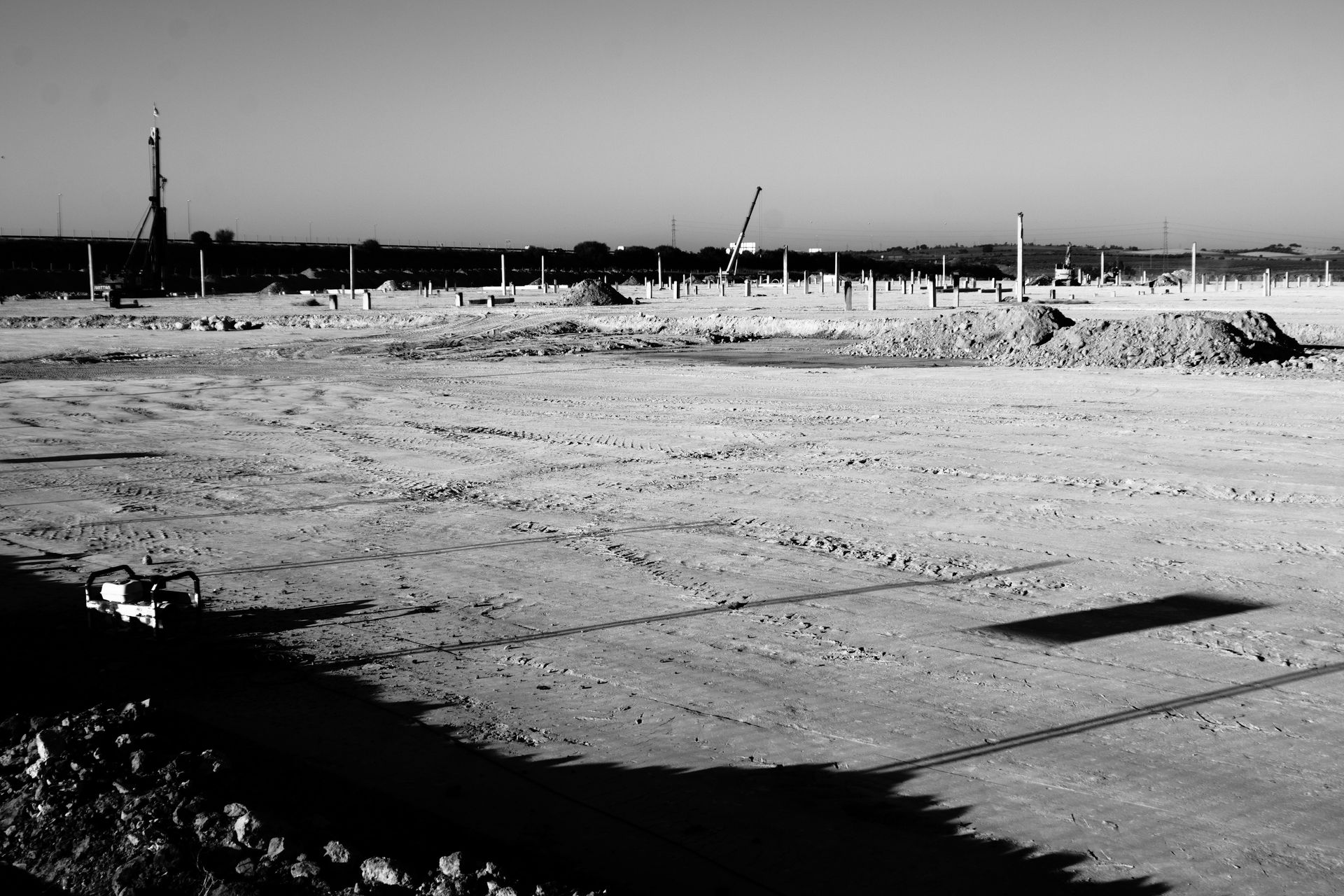 A barren construction site with poles and dirt piles