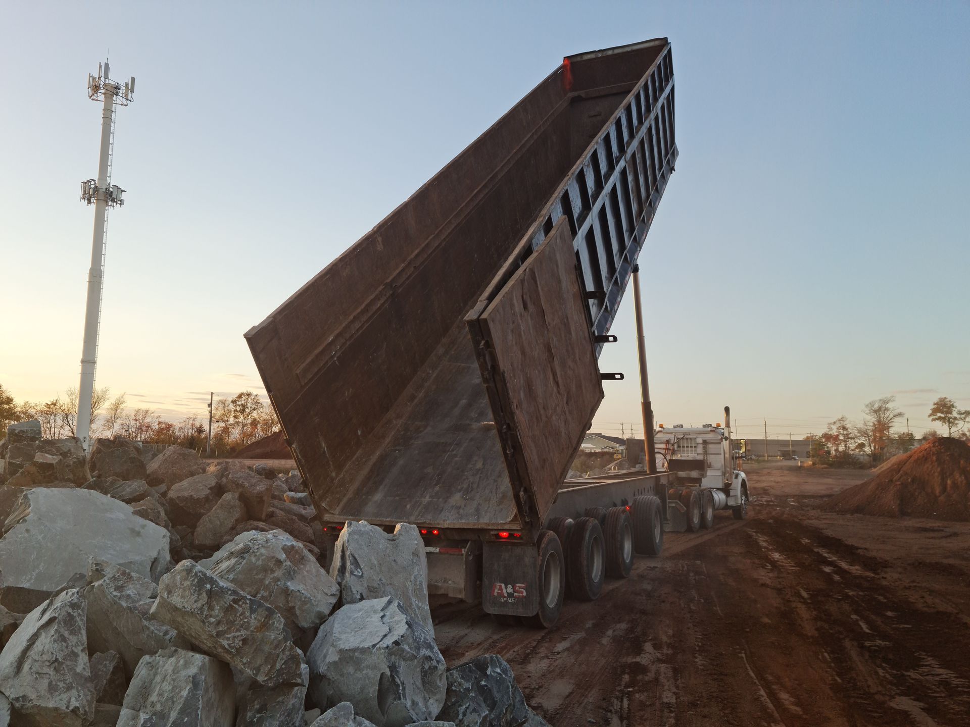 A dump truck unloading rocks at a construction site during sunset.